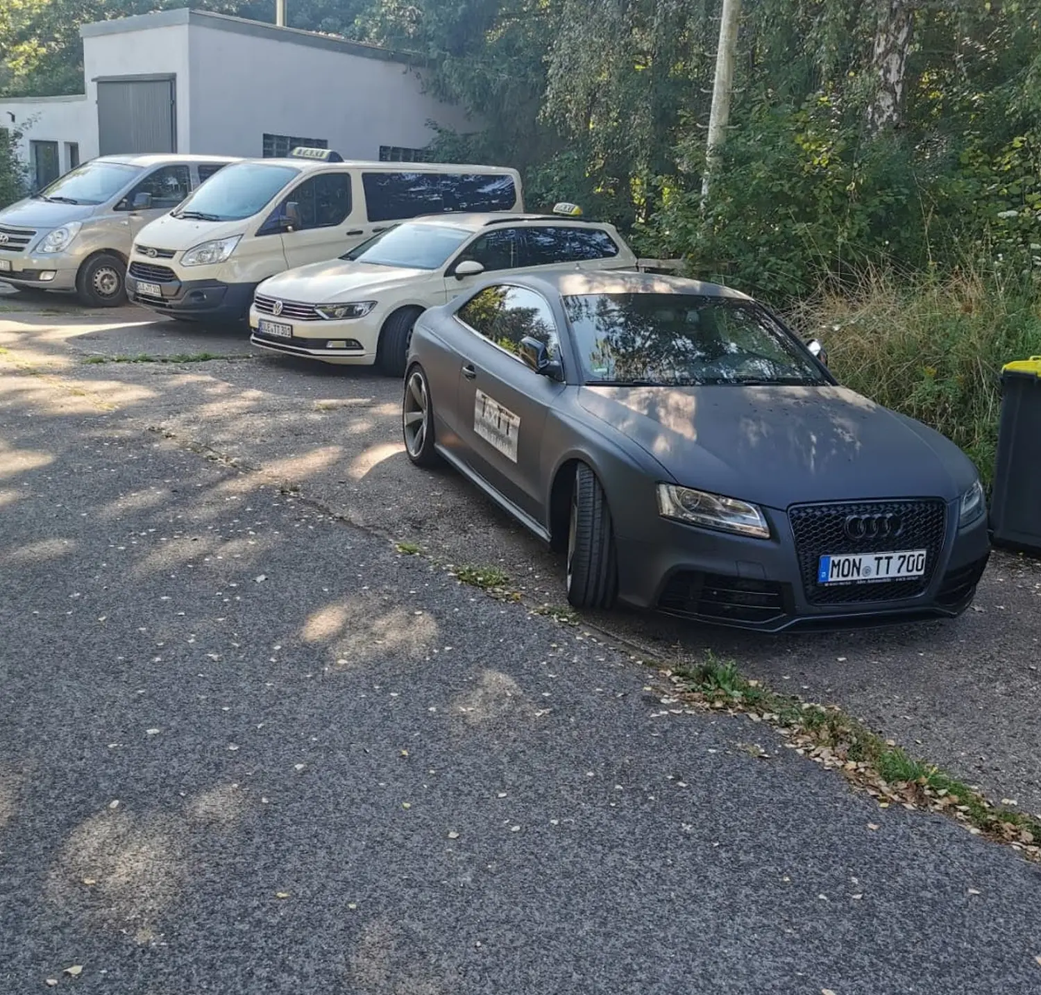 BonChance & TaxiTopTeam GmbH - Transportdienste - Eine dunkelgraue Audi-Limousine mit einem „TAXI“-Schild parkte in einer Reihe von Autos; ein weißer Lieferwagen und ein weiteres weißes Auto waren teilweise zu sehen.